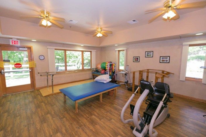 A well-equipped physical therapy room with exercise equipment and a treatment bed.
