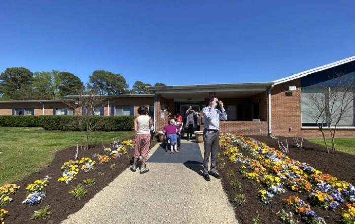 A group of people walking along a pathway lined with colorful flowers on a sunny day.