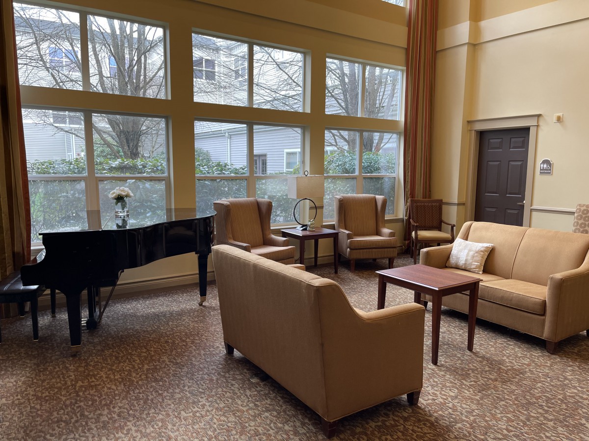 A cozy living room with a grand piano, sofas, and large windows allowing natural light.