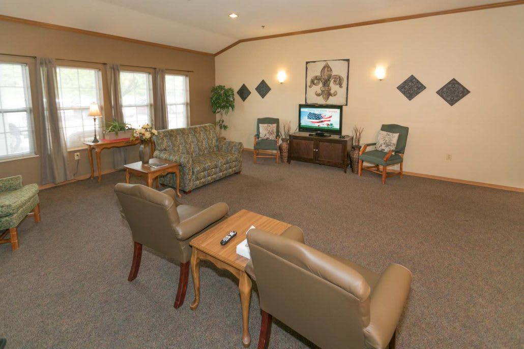 A cozy living room with comfortable seating and a television, featuring large windows and decorative artwork.