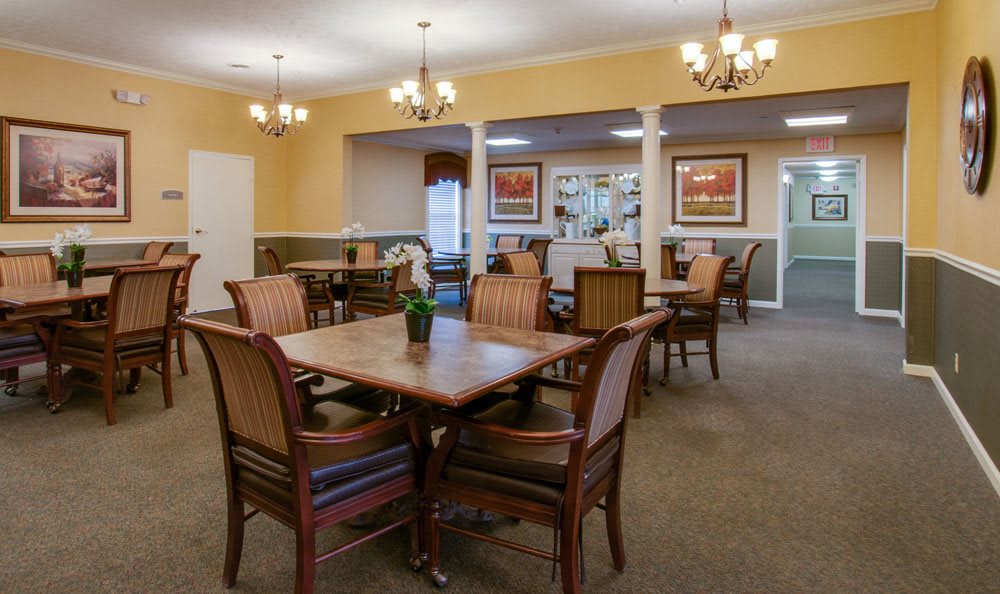 A well-furnished dining room with multiple tables and chairs, accented by chandeliers and wall art.