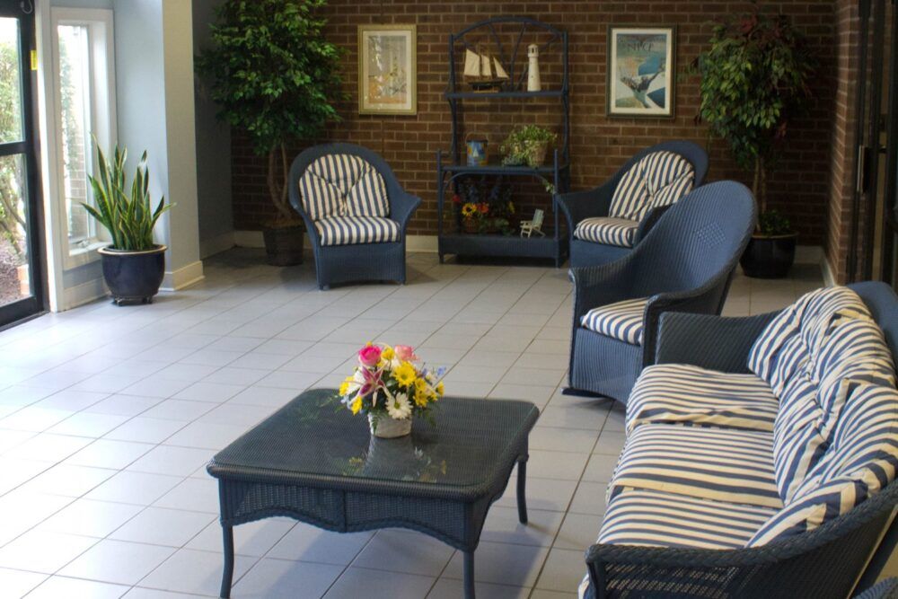 A cozy indoor lounge area featuring wicker furniture with striped cushions and a coffee table adorned with a floral centerpiece.