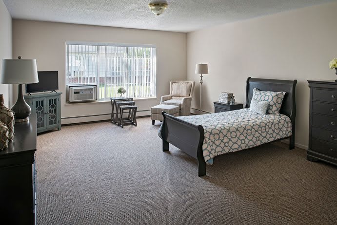 A spacious bedroom with a single bed, chair, and large window letting in natural light.