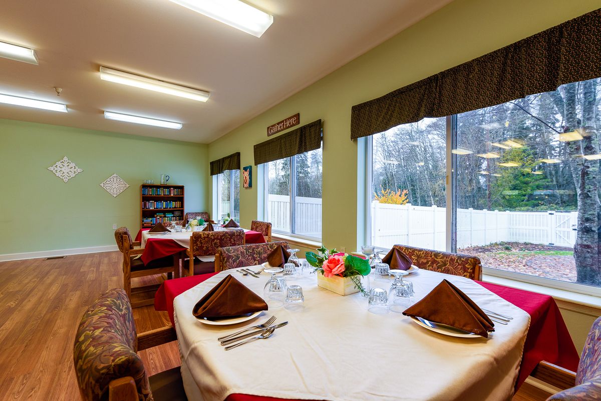 A cozy dining room with elegantly set tables and large windows offering a view outside.