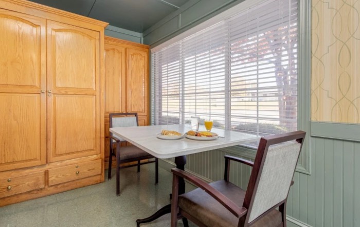 A cozy kitchen nook featuring a table set for breakfast with two chairs and a large window with blinds.