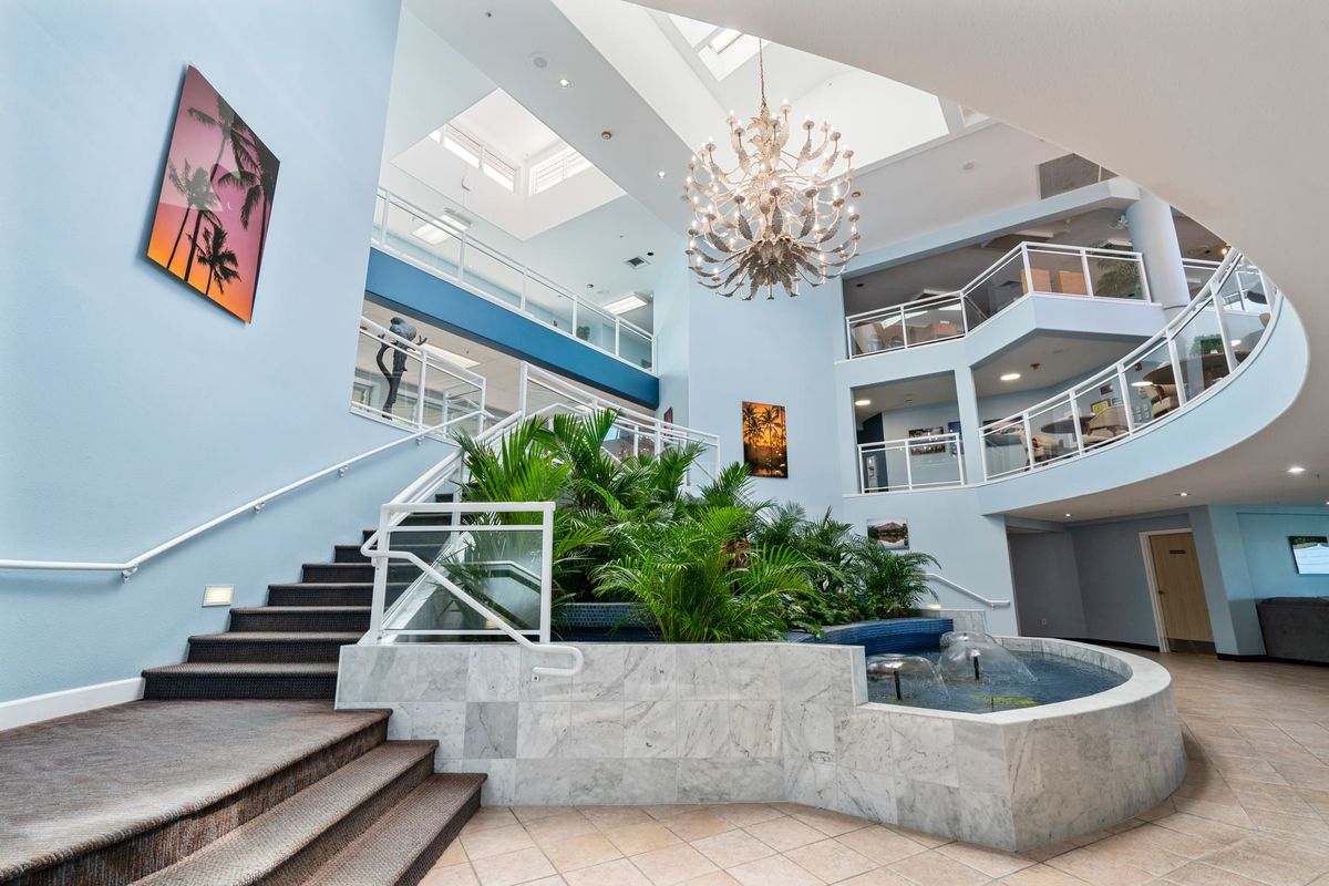 A modern interior space with a central staircase, lush plants, and a striking chandelier under natural light.