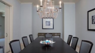 A modern dining room featuring a sophisticated chandelier above a dark wooden table with chairs.