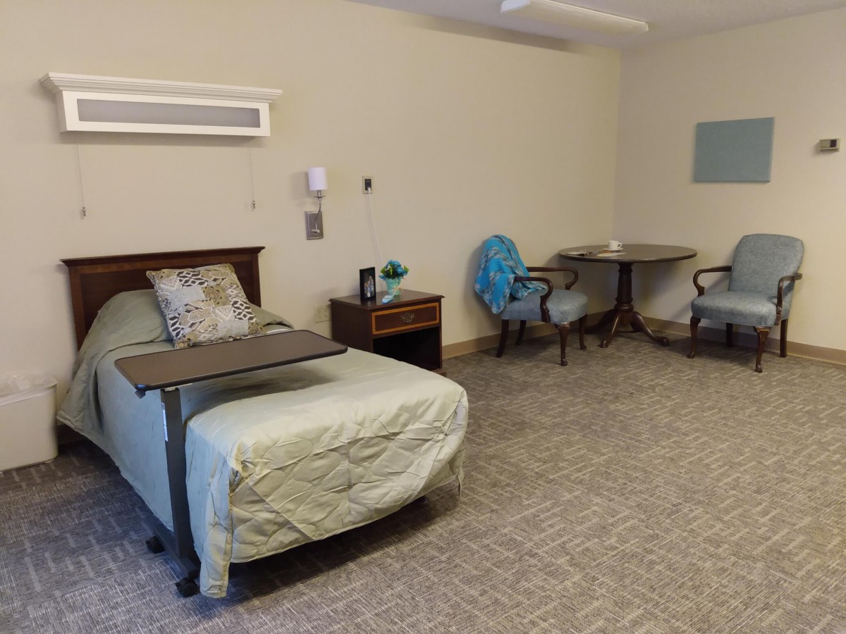 A hospital room with beds, tables, and chairs, featuring a simple and clean design.