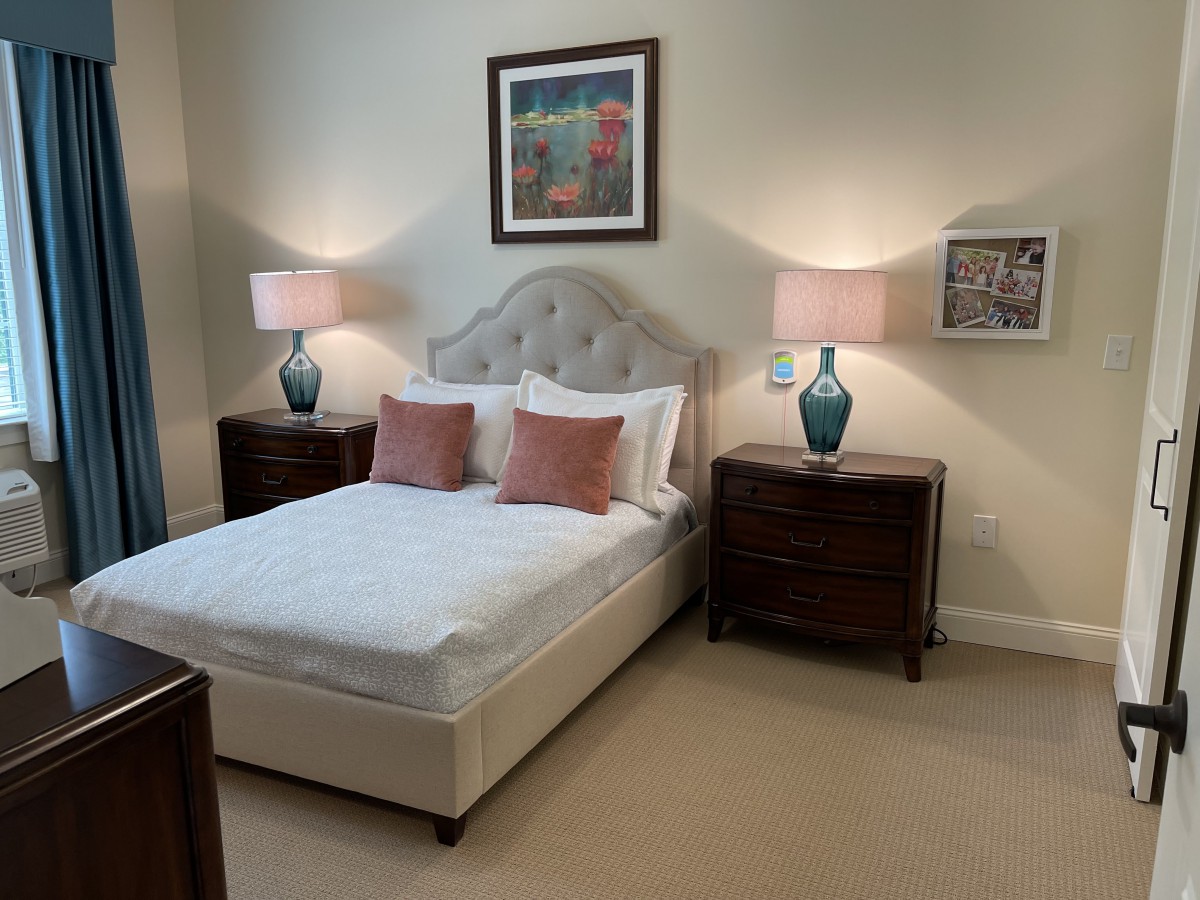 A cozy bedroom with a neatly made bed, flanked by two nightstands and lamps, featuring artwork on the wall.