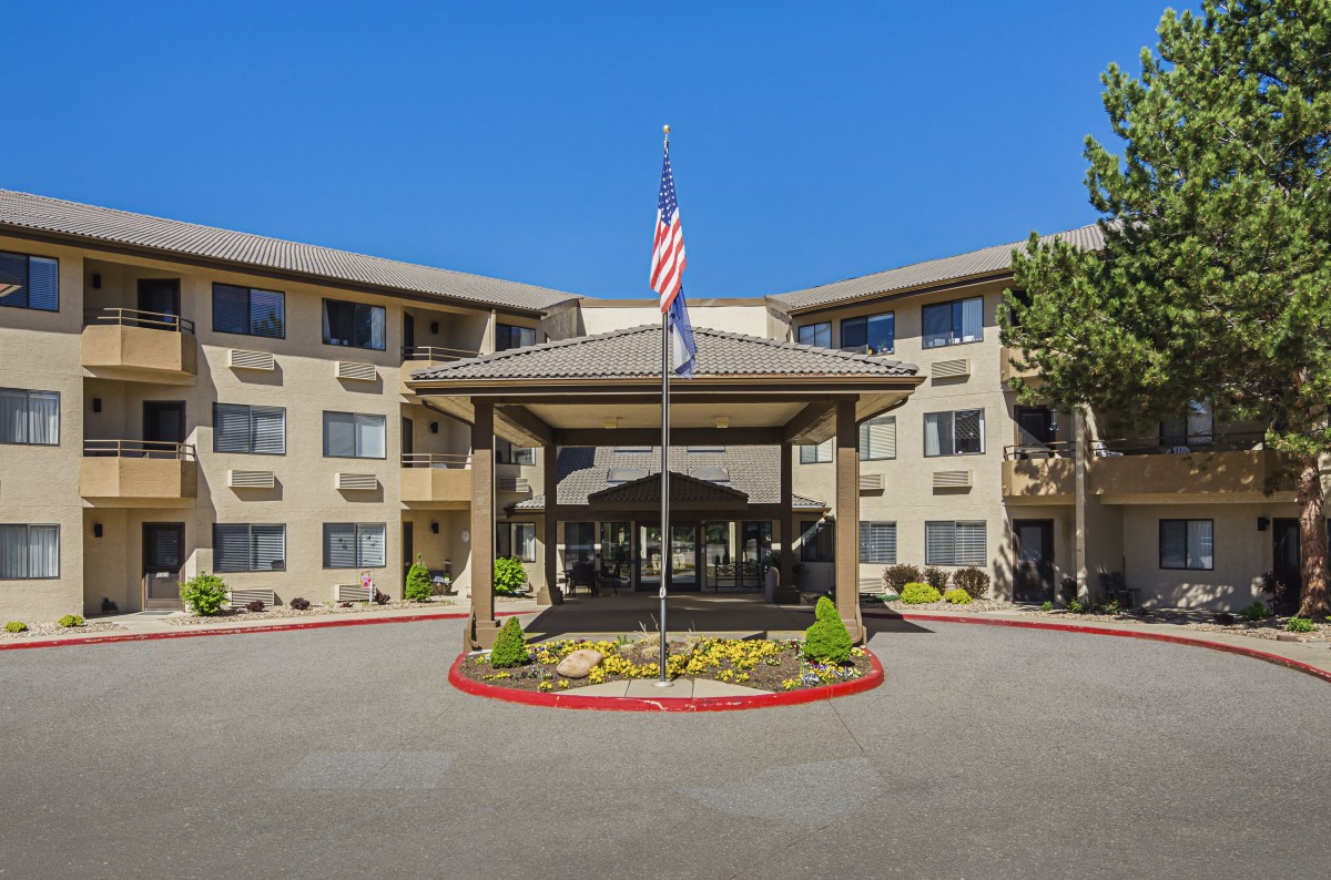 The entrance of a hotel building with an American flag and well-maintained landscaping.