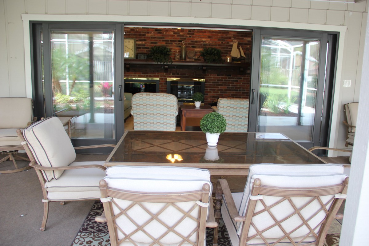 A cozy patio area with a wooden dining table and cushioned chairs, overlooking an indoor space through sliding glass doors.