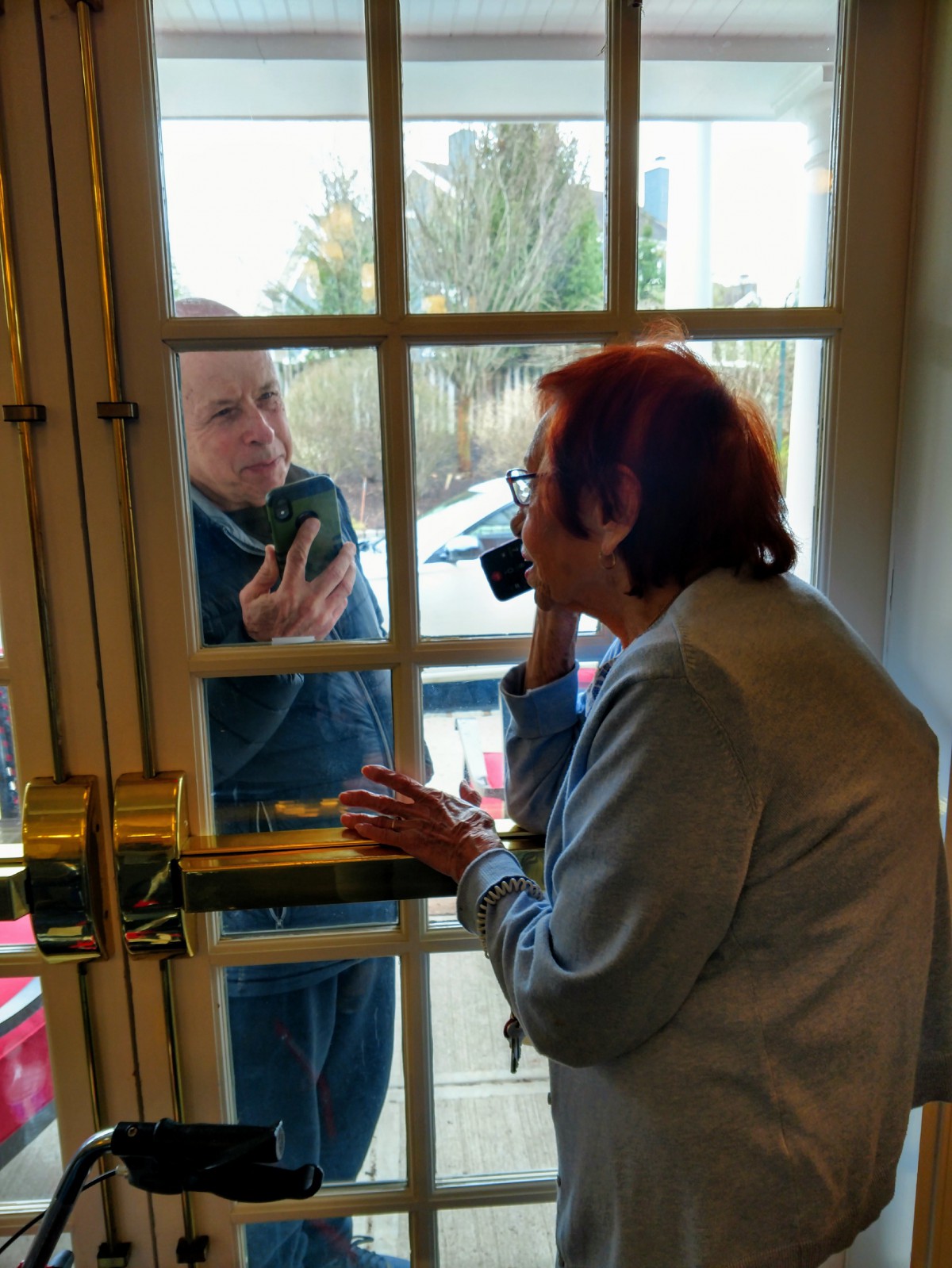 Two people communicating through a glass door.
