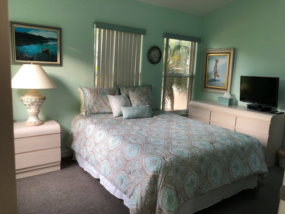 A cozy bedroom with a neatly made bed, paintings on the walls, and soft lighting.