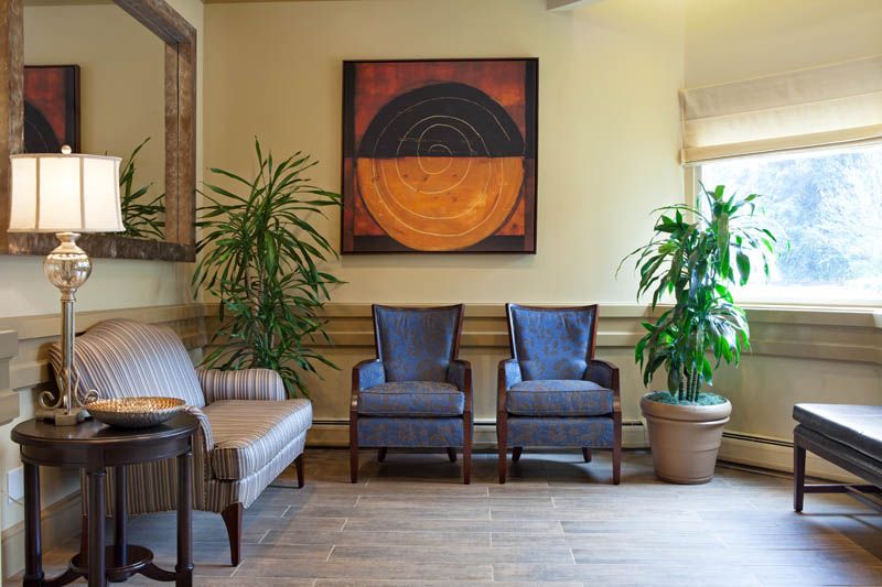 A cozy waiting room with chairs, plants, and abstract artwork on the wall.