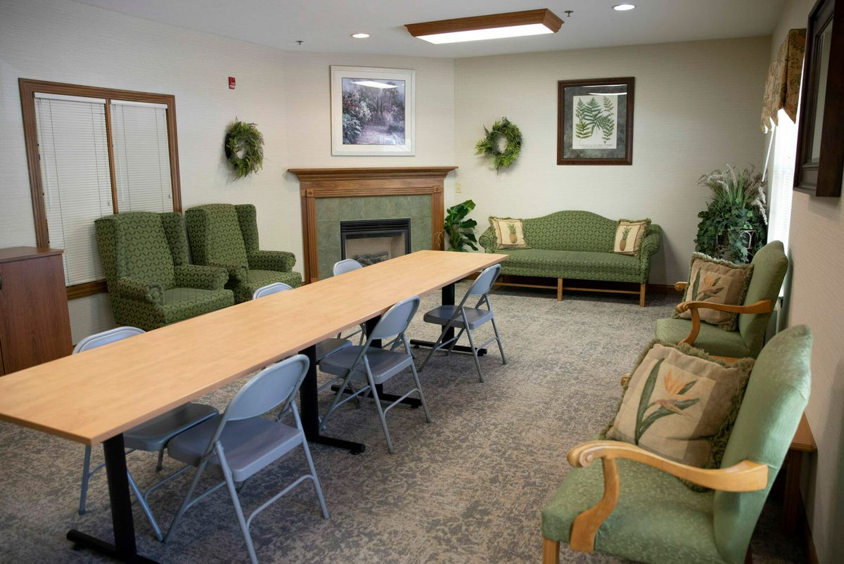 A conference room with a long table, multiple chairs, green seating, and decorative plants.