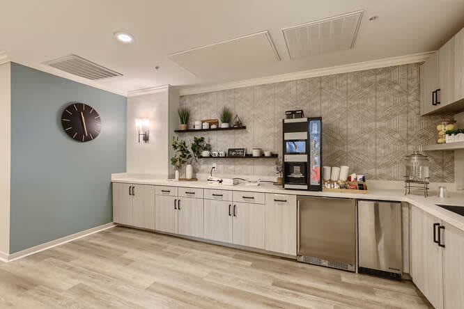 A modern kitchenette with a coffee machine, open shelving, and sleek cabinetry.