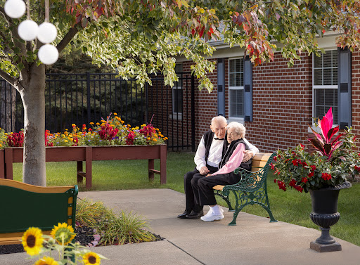 An elderly couple enjoys a serene moment together on a bench surrounded by colorful flowers in an autumn setting.