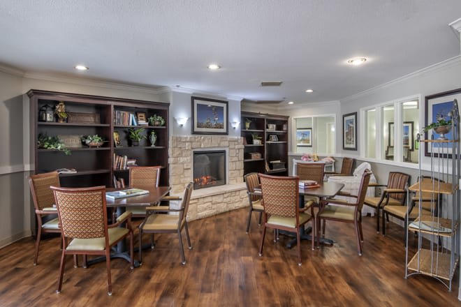 A cozy living room with a fireplace, seating area, and bookshelves on a wooden floor.