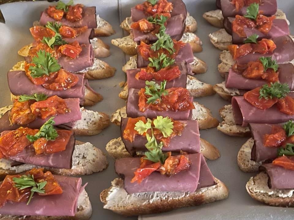 A selection of bruschetta topped with sliced meat, tomatoes, and fresh herbs.