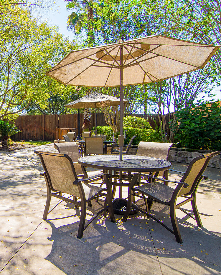 A sunny outdoor patio with a table, chairs, and umbrellas set among greenery.
