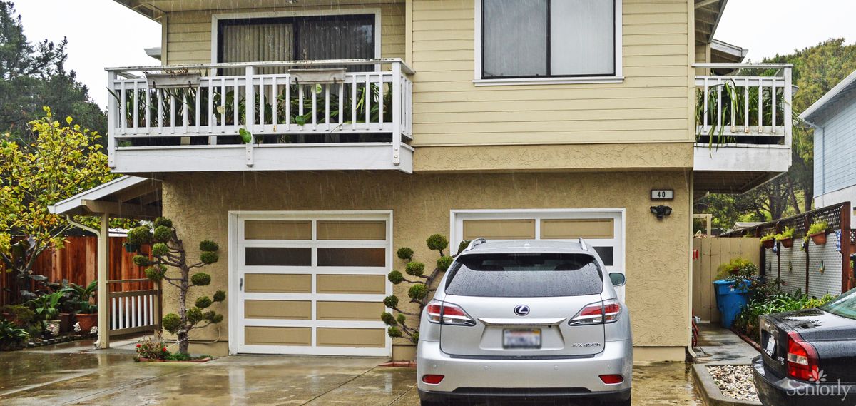 A silver car parked in front of a garage attached to a two-story house with a balcony.