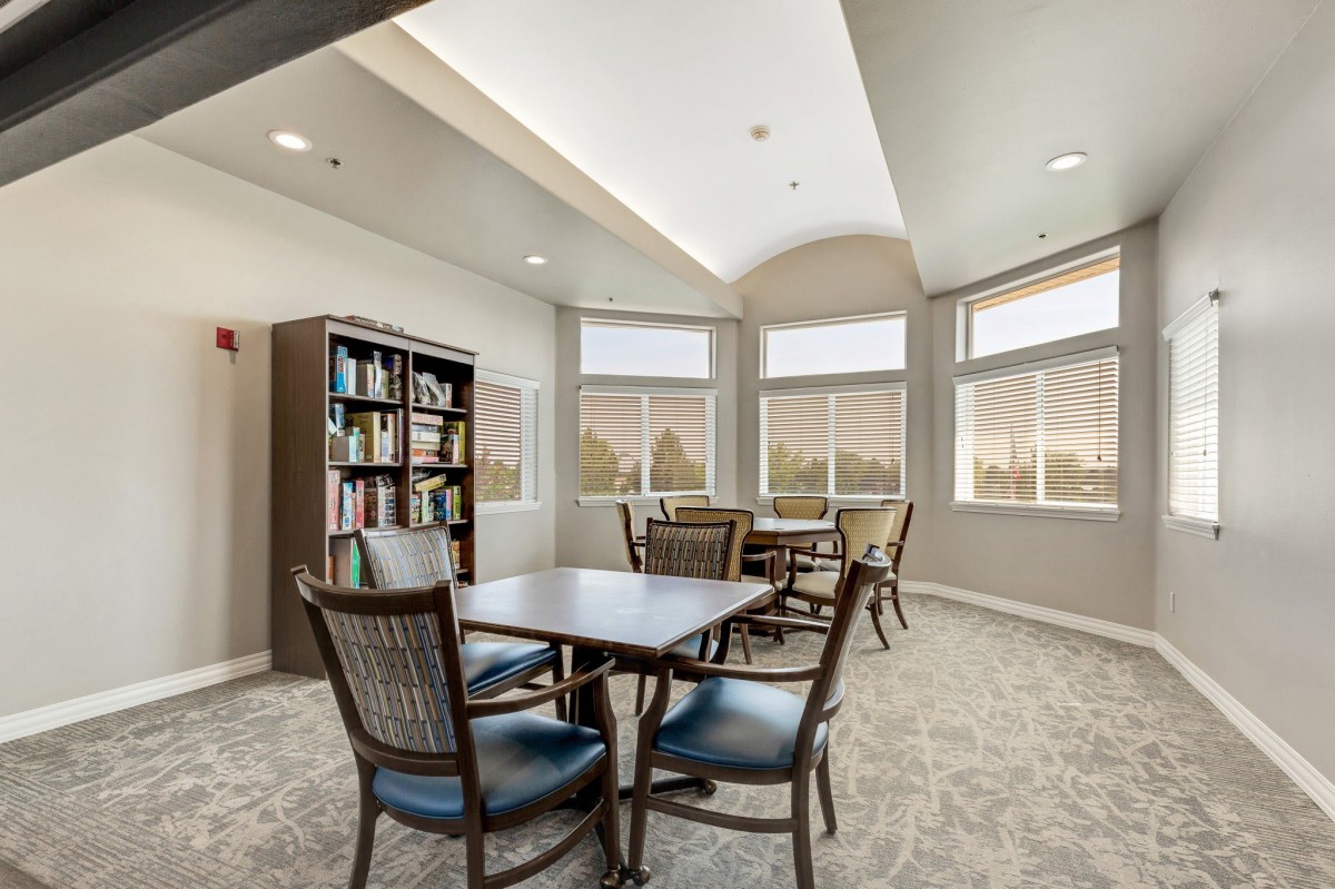A well-lit library room with tables, chairs, and bookshelves.