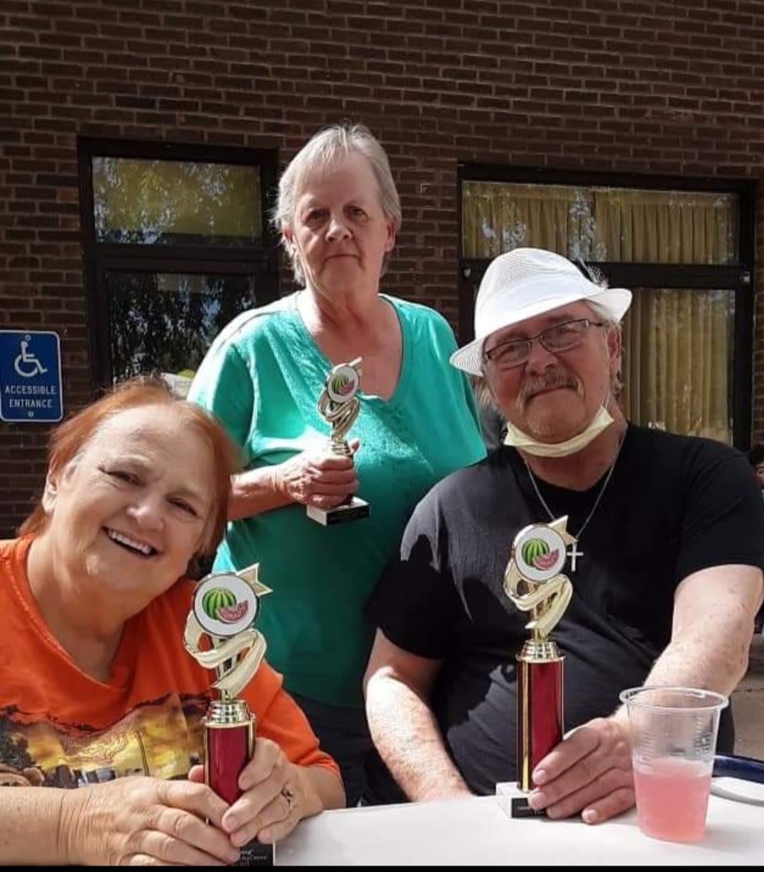 A group of three people holding trophies at an outdoor event.