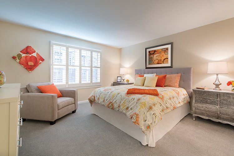 A cozy and modern bedroom featuring a neatly made bed with colorful pillows, an armchair, and artwork on the wall.