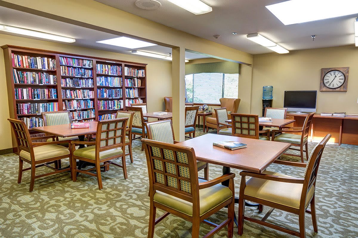 A cozy library reading room with tables, chairs, and bookshelves filled with books.