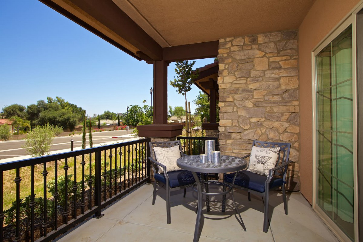 A cozy patio with a small table and two chairs, set against a stone wall on a sunny day.