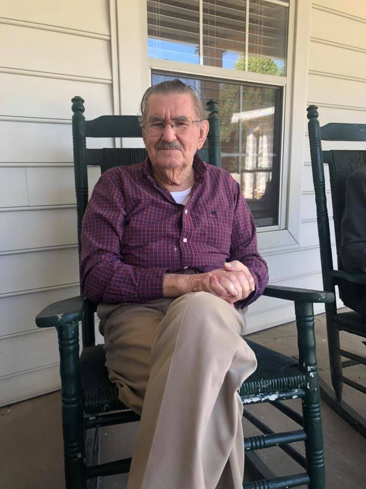 An elderly man sitting on a porch in a rocking chair.