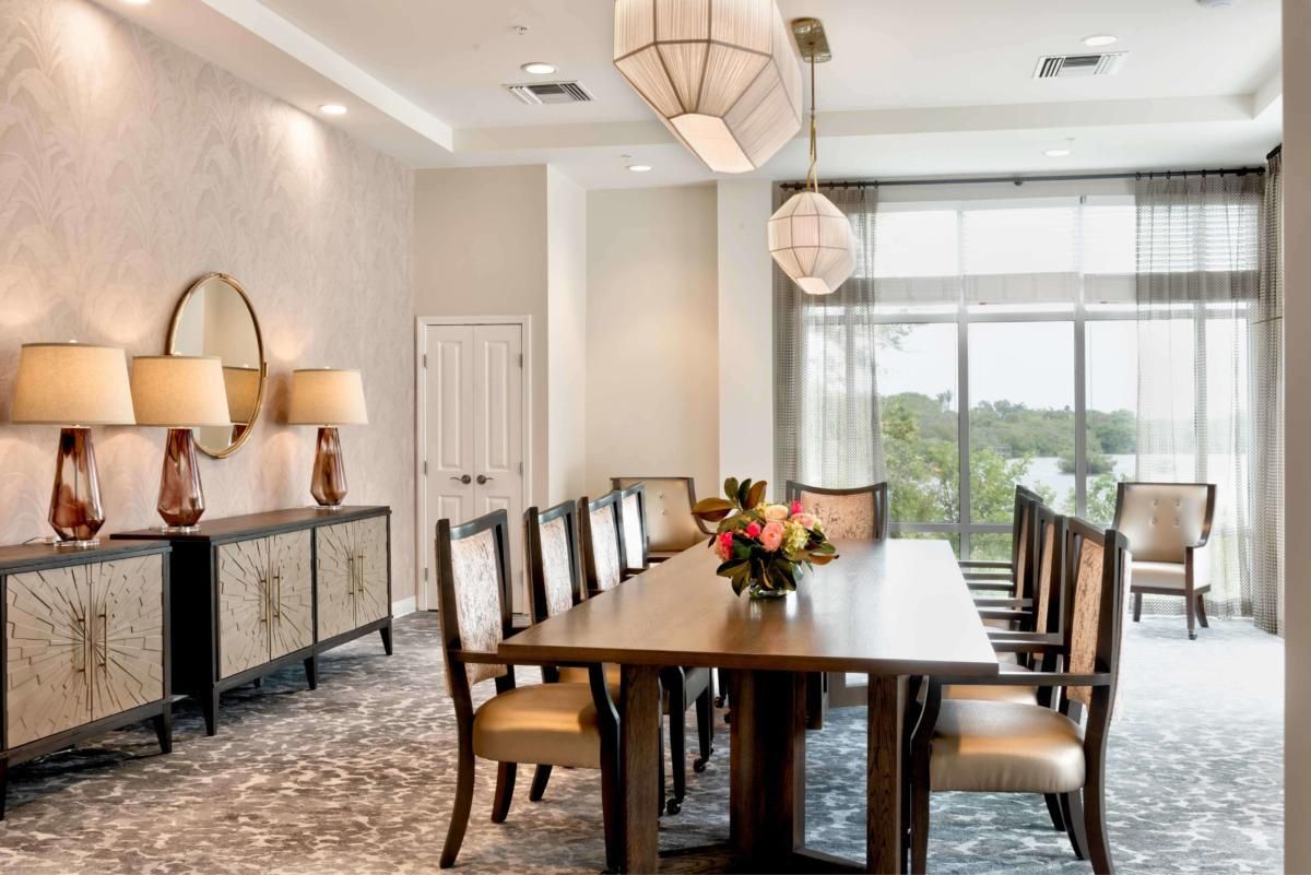 A modern dining room with a long table, elegant chairs, stylish pendant lights, and a window view.