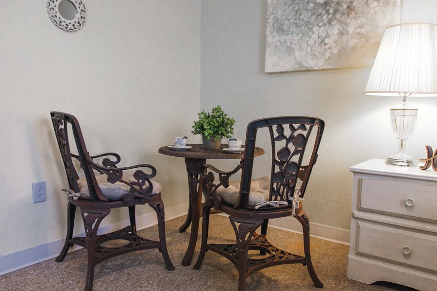 A cozy dining area with a small round table and two ornate chairs, complemented by a potted plant and wall decor.