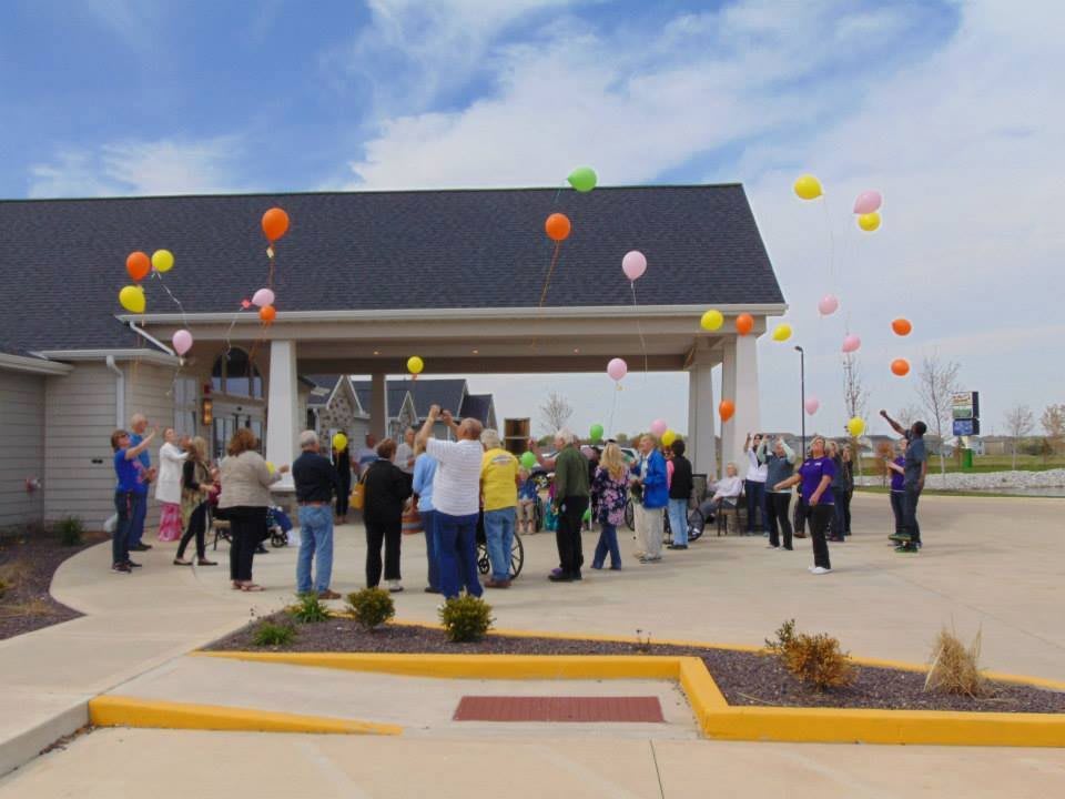 A crowd gathered outside under a pavilion with colorful balloons floating in the sky.