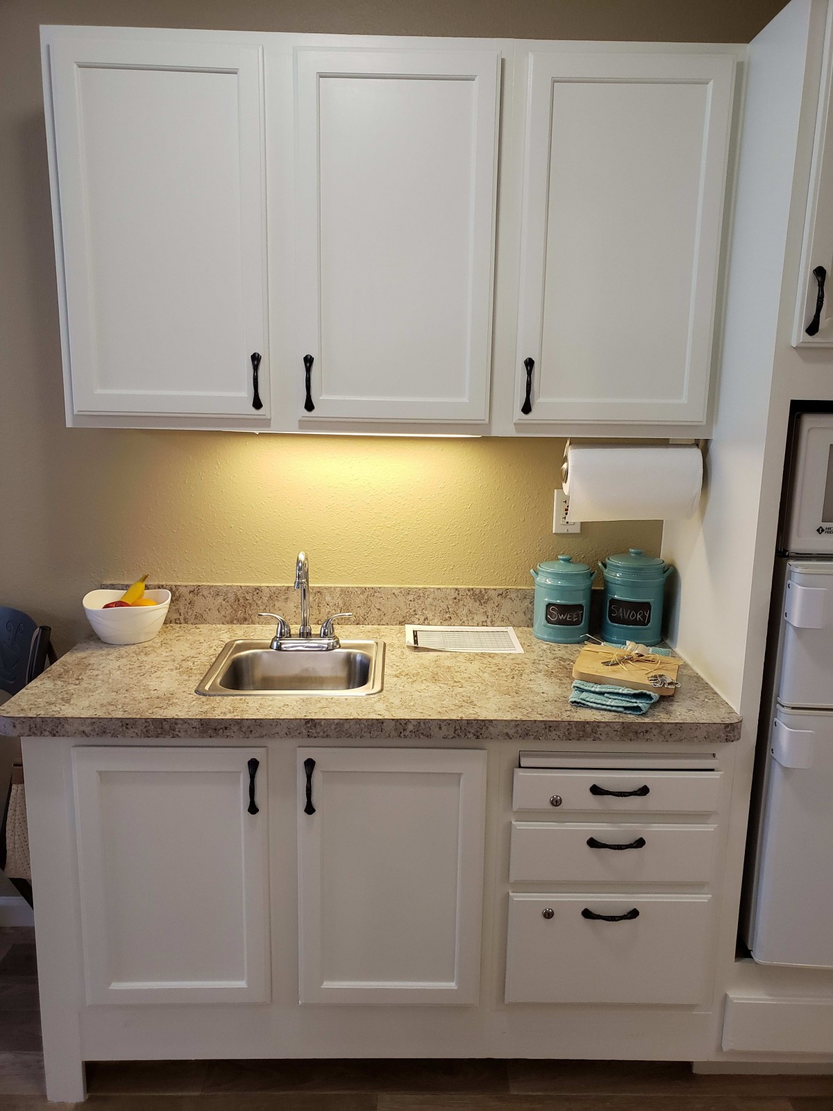 A compact kitchen area with white cabinets, a sink, and countertop accessories.