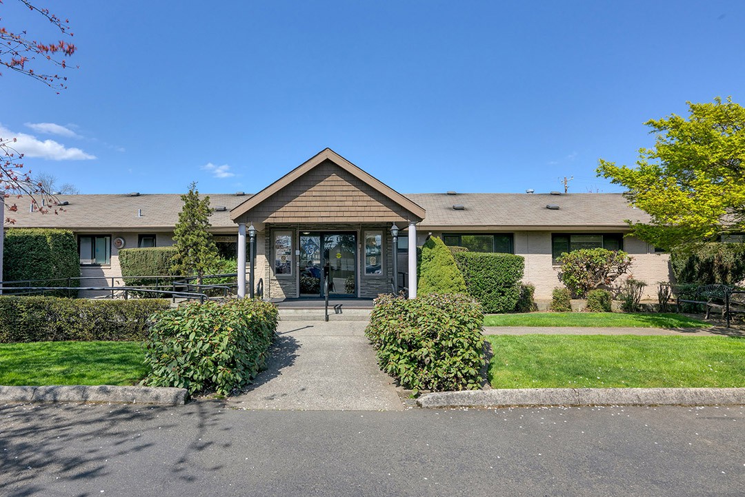 A building with a wooden entrance surrounded by well-maintained greenery and a clear pathway.