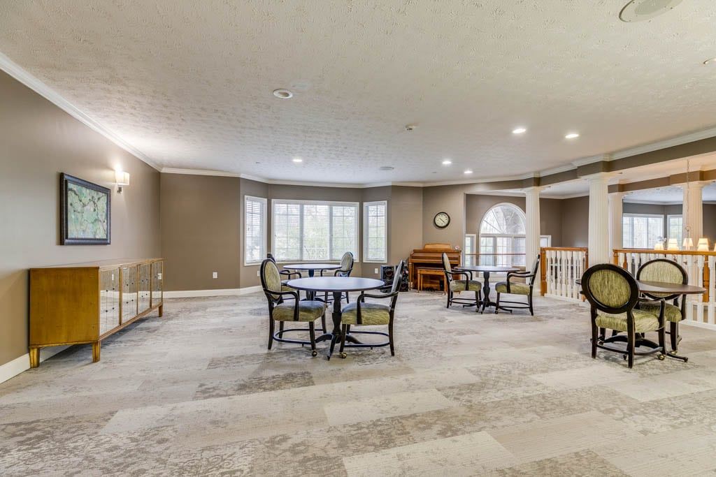 A spacious and well-lit dining area with several tables and chairs, featuring large windows and a neutral color palette.