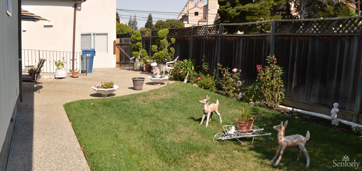 A peaceful backyard with a lush green lawn, decorated with plants and a deer statue.