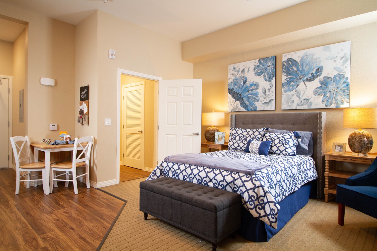 A cozy bedroom featuring a neatly made bed with blue and white patterned bedding, complemented by artwork on the walls.