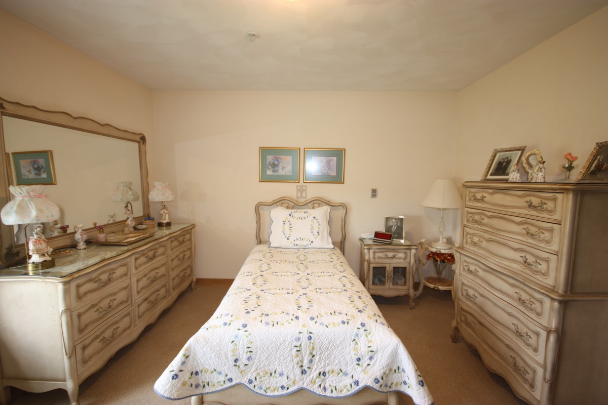 A cozy bedroom with vintage furniture featuring a single bed, dresser, mirror, and side table.