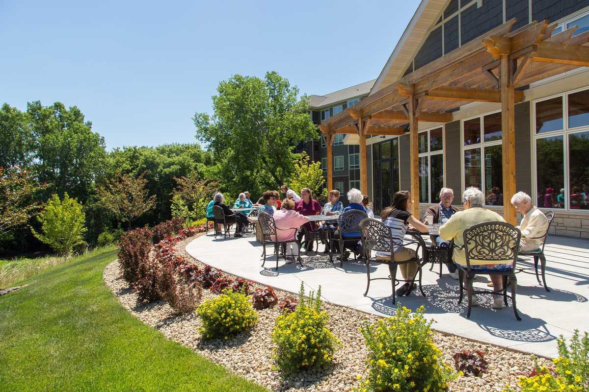 A group of people enjoying a sunny day on a patio with garden views.