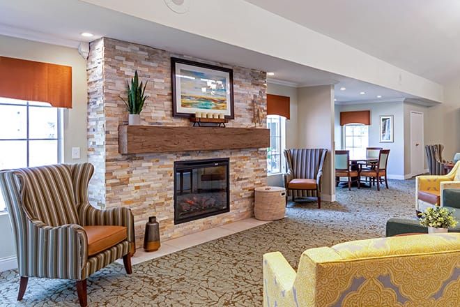 A cozy living room with a stone fireplace, featuring comfortable armchairs and elegant decor.