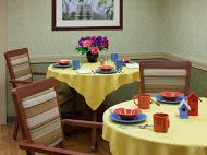 A dining area with tables set for a meal, featuring yellow tablecloths, colorful dishware, and a floral centerpiece.