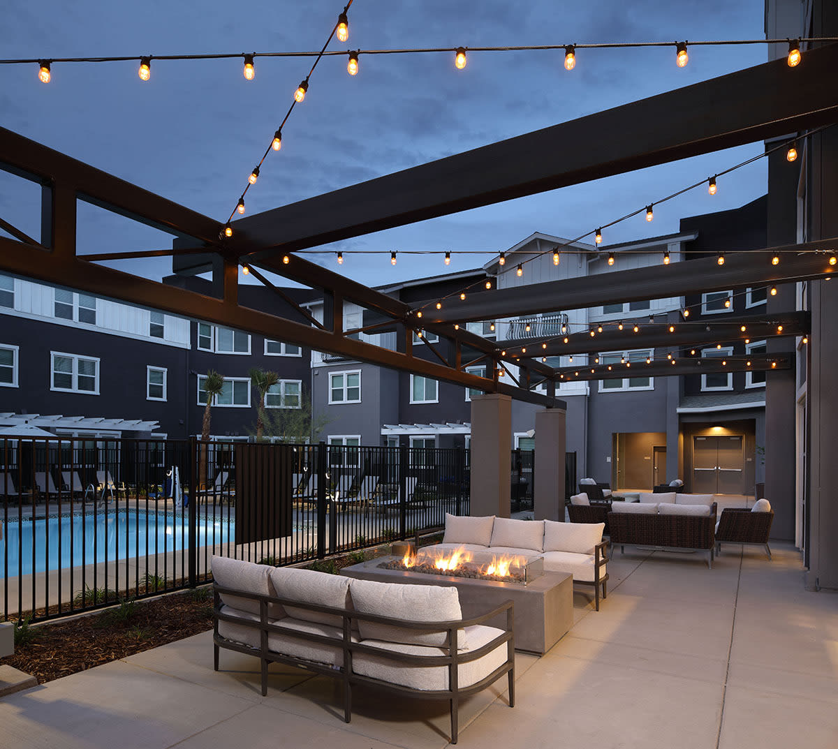 Modern outdoor patio with comfortable seating and string lights by a pool.