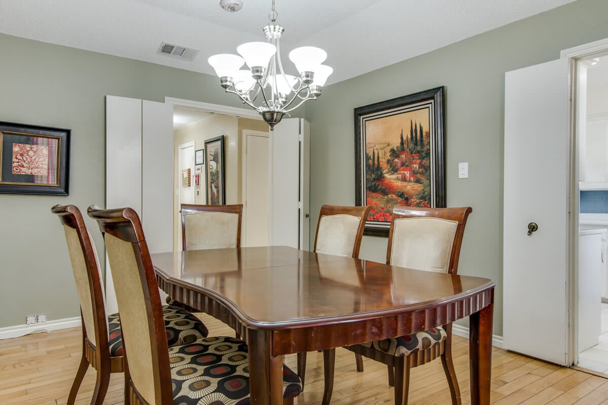 A dining room with a wooden table, upholstered chairs, a chandelier, and wall art.