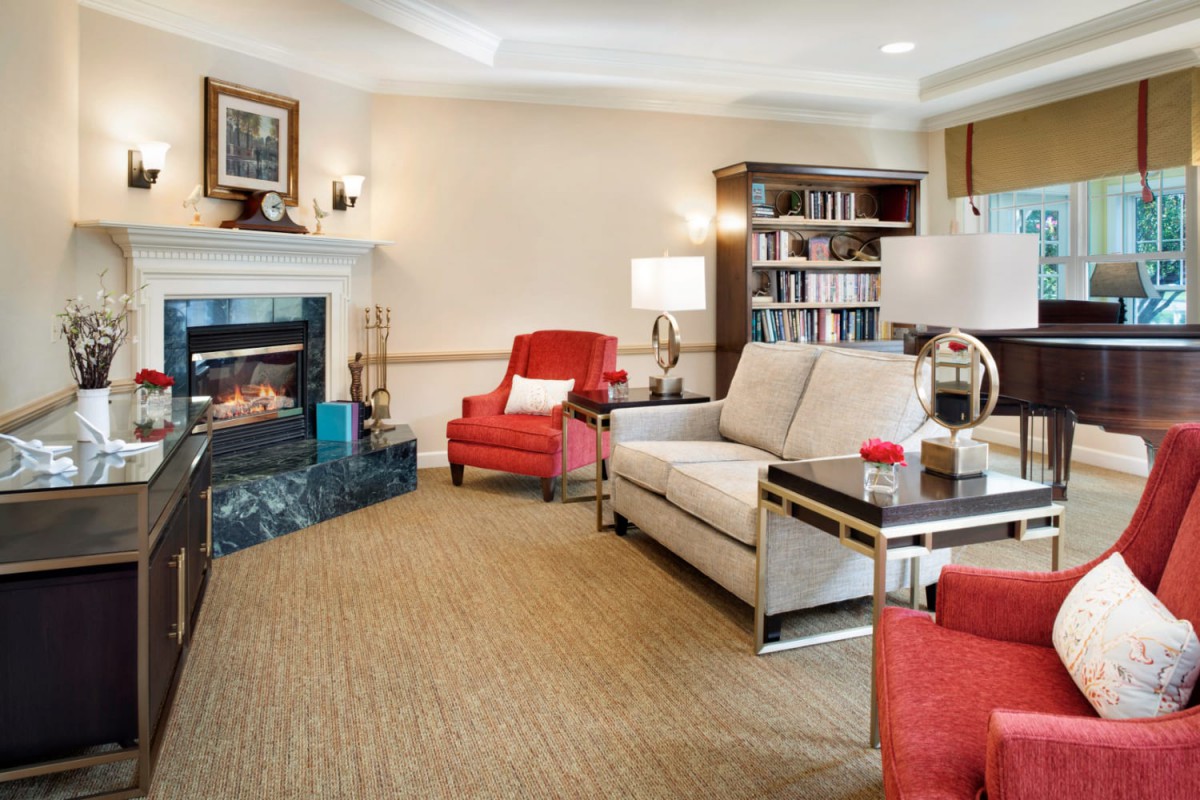 A cozy living room with a fireplace, red armchairs, a beige sofa, and a bookshelf.