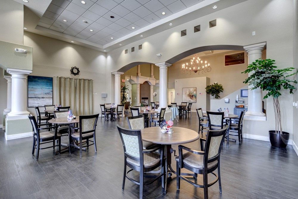 A spacious and elegantly decorated dining area with multiple tables and chairs, illuminated by a chandelier.