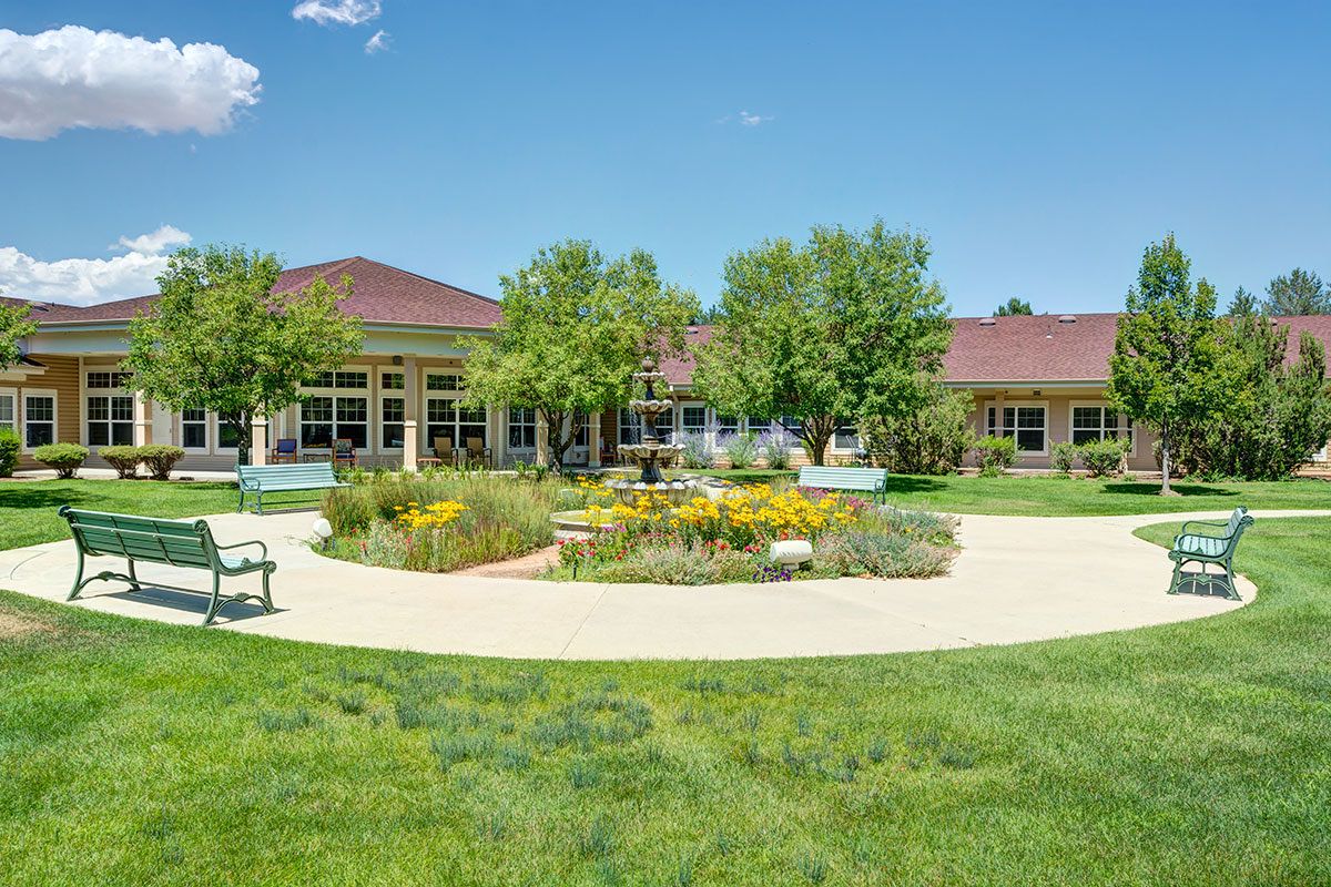 A landscaped garden with a pathway, benches, and a building in the background.