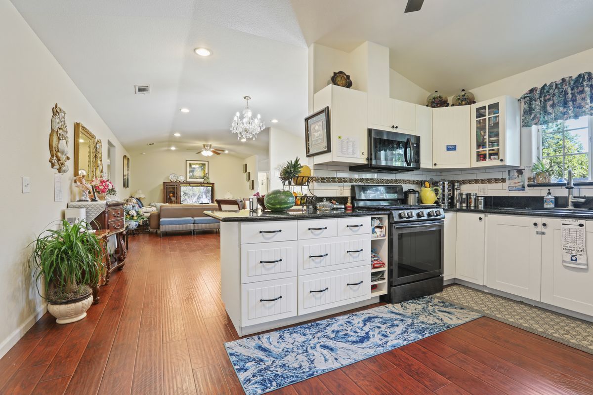 A modern open-concept kitchen and living area featuring white cabinetry, wooden flooring, and contemporary appliances.