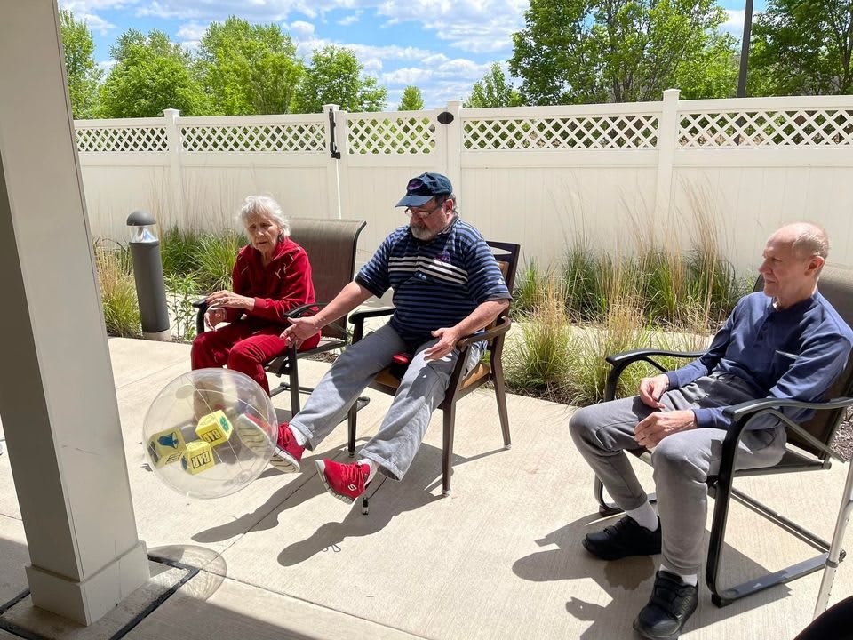 A group of people sitting outdoors near a white fence, enjoying a sunny day.